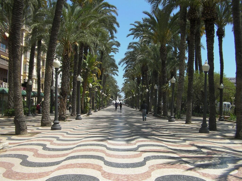 Dlážděná promenáda Explanada de España v Alicante lemovaná palmami, v dálce několik chodců