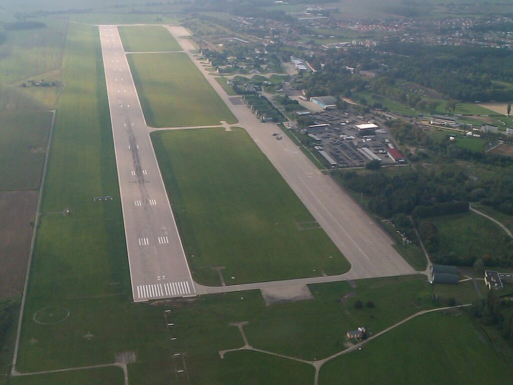 Letecký pohled na dráhu a plochu Letiště Pardubice s areálem a přilehlou zástavbou